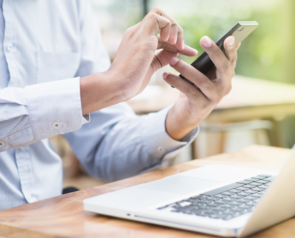 image of hands texting on a smartphone with a laptop on a table